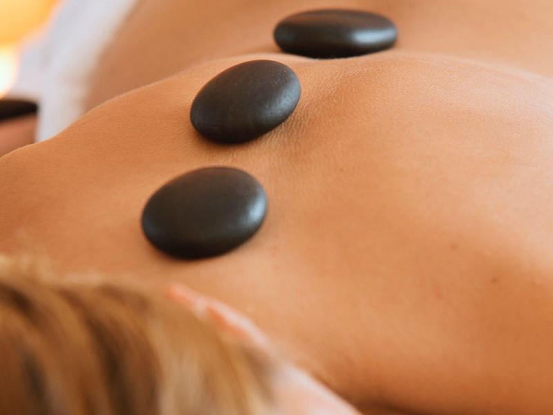 Person receiving hot stone massage with three black stones on the back.