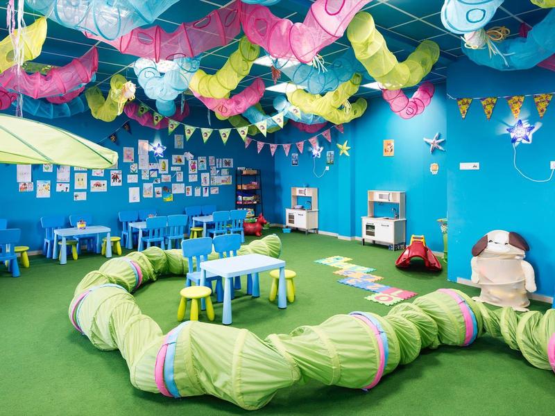Colorful playroom with blue walls, green climbing tunnel, and colorful decorations on the ceiling.