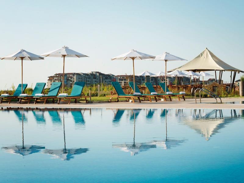 Pool with lounge chairs and umbrellas at a hotel under clear sky.