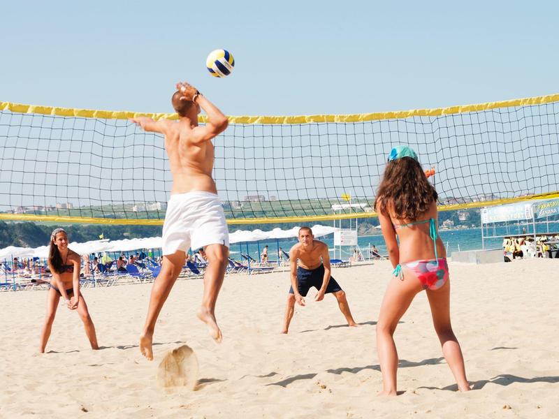 People playing volleyball on the beach under sunny, clear skies.