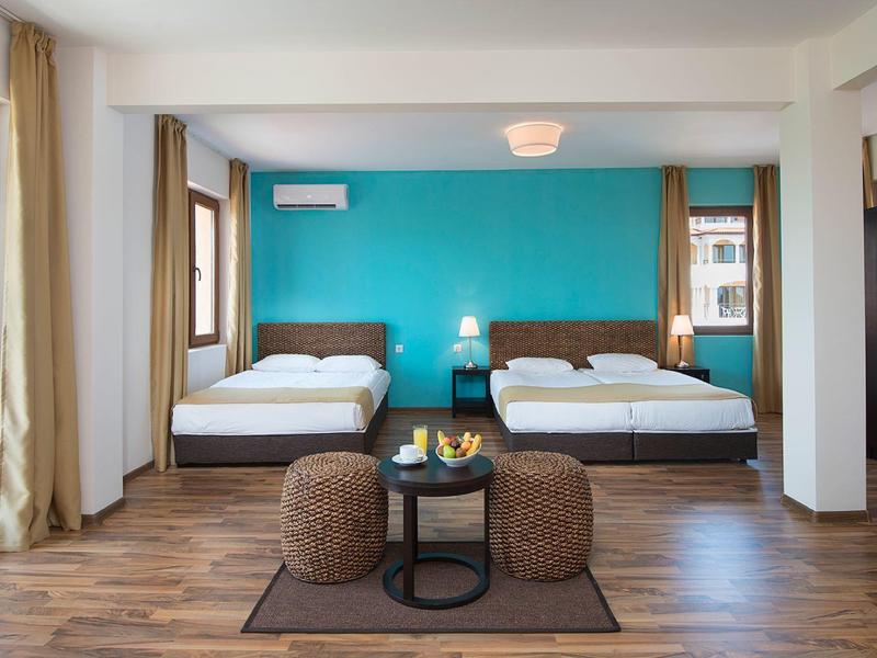 Spacious hotel room with two single beds, blue accent wall, and balcony with a view.