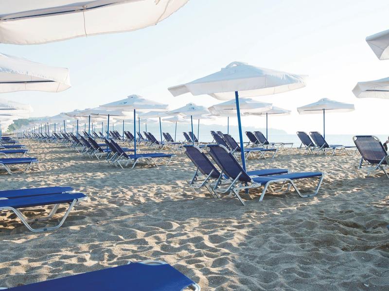 Row of blue lounge chairs with white umbrellas on sandy beach