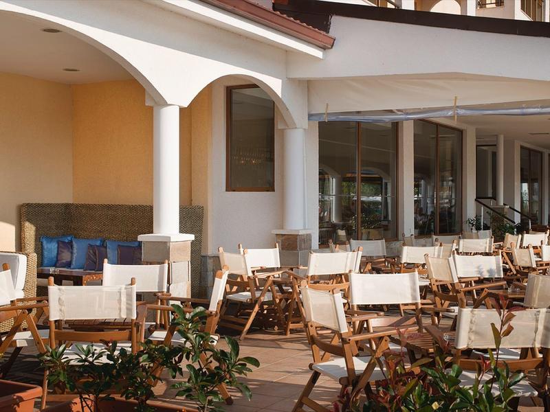 Large terrace with many white chairs and tables in front of a hotel building in daylight.