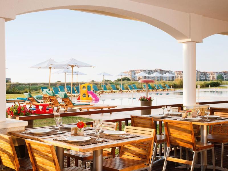 Covered terrace with dining tables overlooking a lake with a water playground.