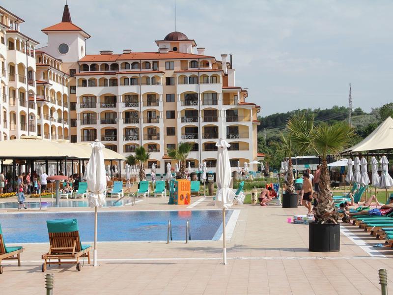 Large hotel with pool, sun loungers, and umbrellas in a sunny setting