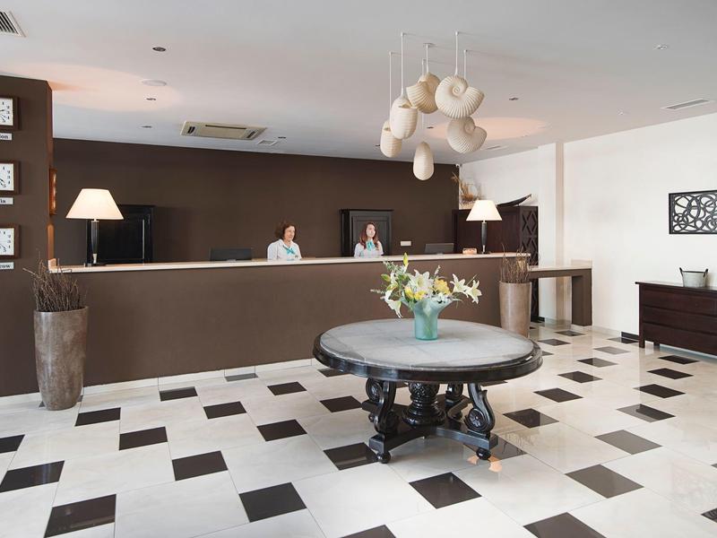 Modern hotel reception area with round table, flowers, and two reception staff.