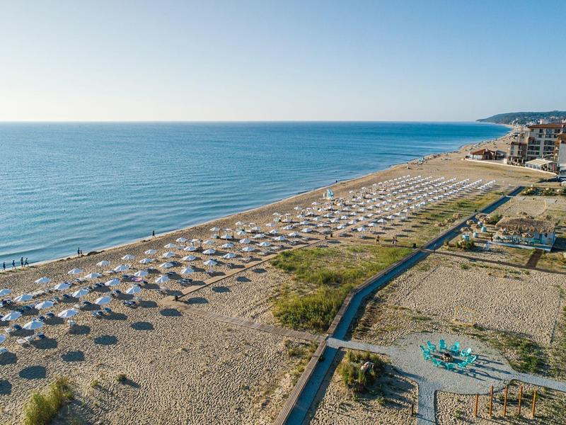 Long sandy beach with sun umbrellas and nearby hotels by the sea.