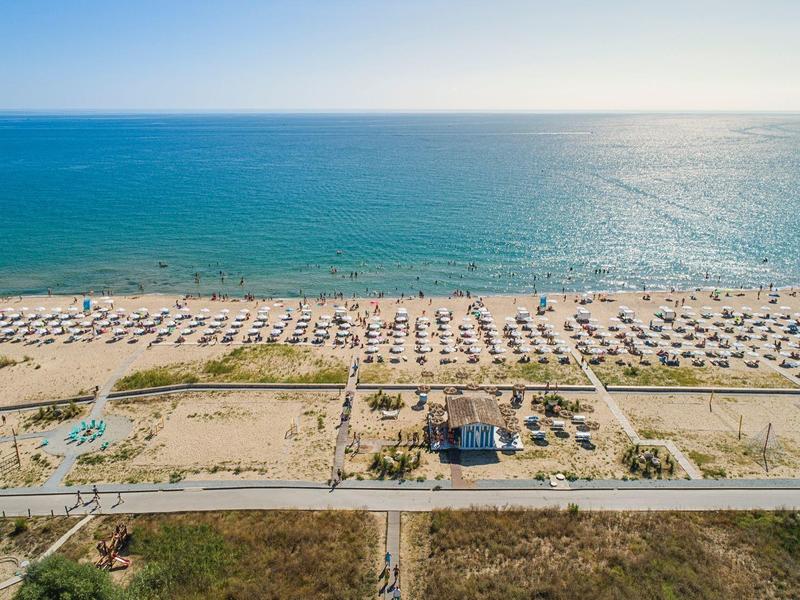 Aerial view of a wide beach with sun umbrellas and loungers by the sea.