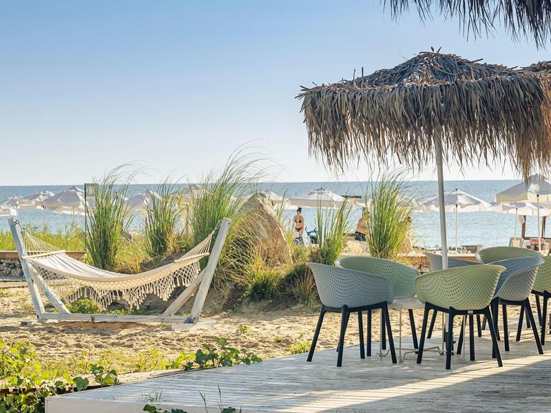 Beach café with chairs, hammock, and shaded parasol overlooking the sea.