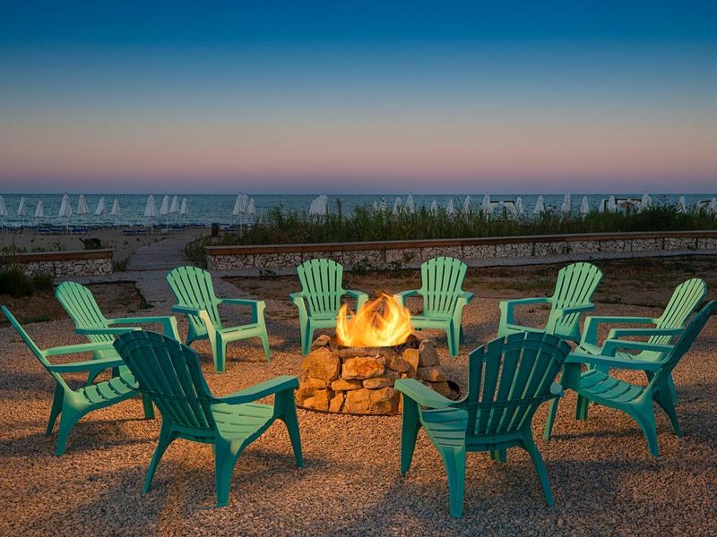 Cozy fire pit with green chairs on gravel near the sea at dusk