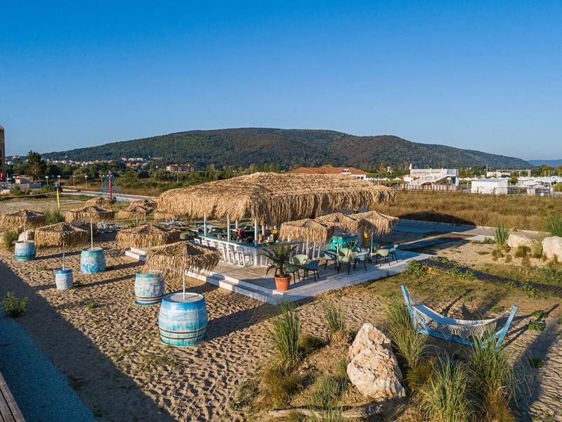Beach area with beach chairs and a large straw roof under a blue sky.