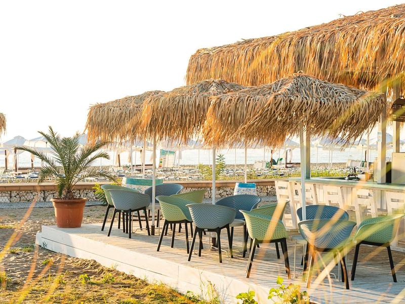 Hotel outdoor area with tables, chairs, and thatched roofs on a sunny day.