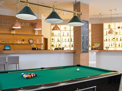 Ein moderner Hotelbarbereich mit Billardtisch und beleuchteten Regalen im Hintergrund.