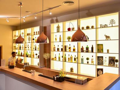 Helle Hotelbar mit modernen Pendelleuchten und beleuchteten Regalen voller Flaschen und Dekorationen.