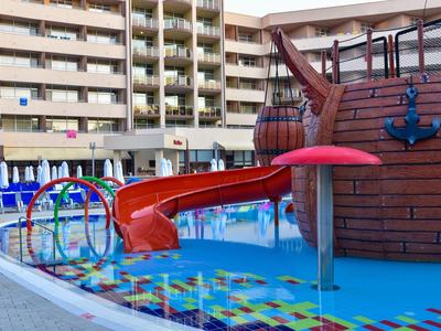 Barevné vodní hřiště s tobogánem a pirátskou lodí vedle balkónů hotelu