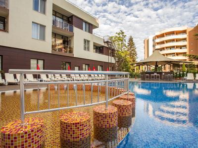 Moderner Außenpool mit bunten Barhockern und Liegestühlen vor Hotelgebäuden bei bewölktem Himmel.