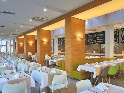 Helles Restaurant mit weißen Tischdecken, grünen Stühlen und Holzpaneelen an den Wänden.