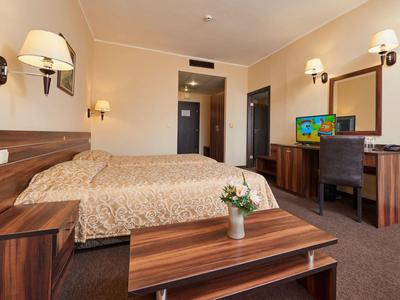 Hotelový pokoj se dvěma jednolůžky, dřevěným nábytkem a televizí na psacím stole.