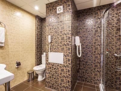 Moderní hotelová koupelna s hnědým vzorovaným sprchovým koutem, toaletou a bílým ručníkem.