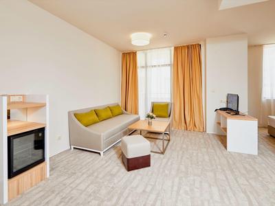 Světlý hotelový pokoj se sedačkou, konferenčním stolkem, TV, postelí a minibarem v čistém, prostorném pokoji.