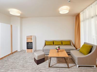 Světý hotelový pokoj se dvěma šedými pohovkami, konferenčním stolkem a velkými okny se závěsy.