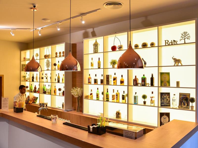 Moderní hotelový bar s teplým osvětlením a policemi s lahvemi a dekoracemi.