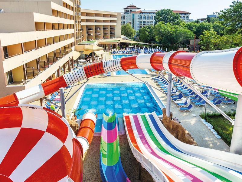 Vodní skluzavky vedoucí k velkému bazénu obklopenému lehátky a stromy.