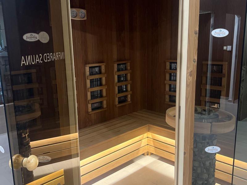 Dřevěná sauna se skleněnými dveřmi a nepřímým osvětlením pod lavičkou.