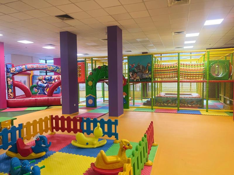 Barevné vnitřní hřiště s klouzačkami, prolézačkami a nafukovacími překážkami ve velké hale.