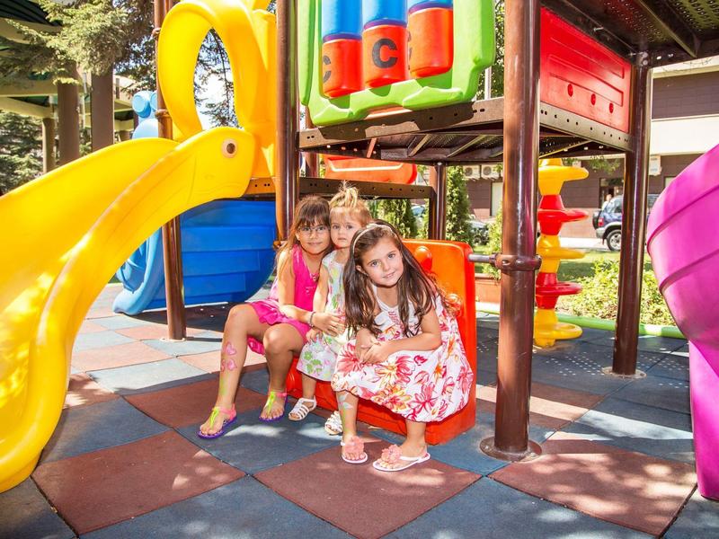 Děti si hrají na barevném hřišti se skluzavkami na slunném venkovním prostranství.