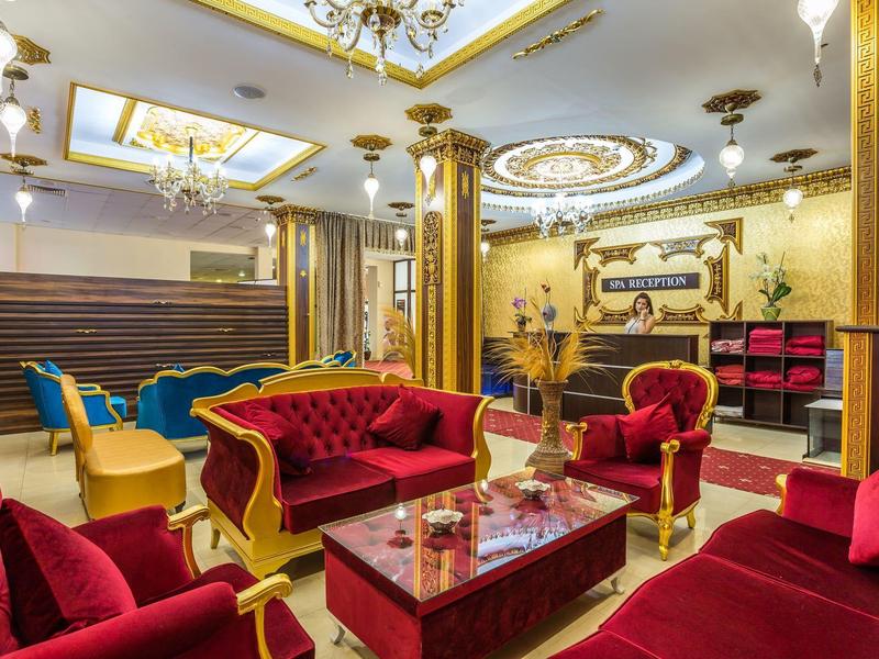 Luxusní hotelová lobby s červenými sametovými pohovkami, zlatými sloupy a zdobeným stropem.