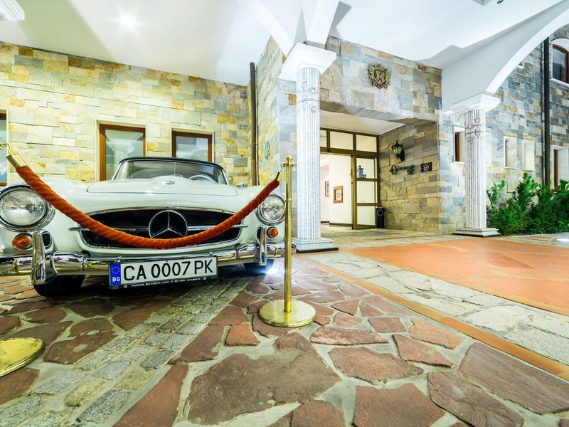 Klassisches silbernes Auto vor Haus mit Natursteinwänden und rotem Pflasterweg.