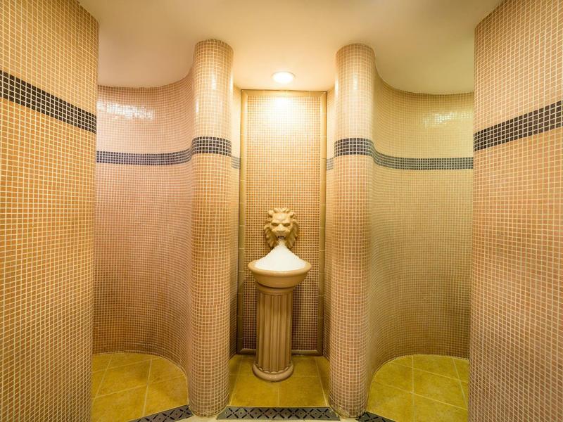 Sanitärbereich mit zwei Plastiktüren, gelbbraunen Kacheln und dekorativer Säule mit Vase.