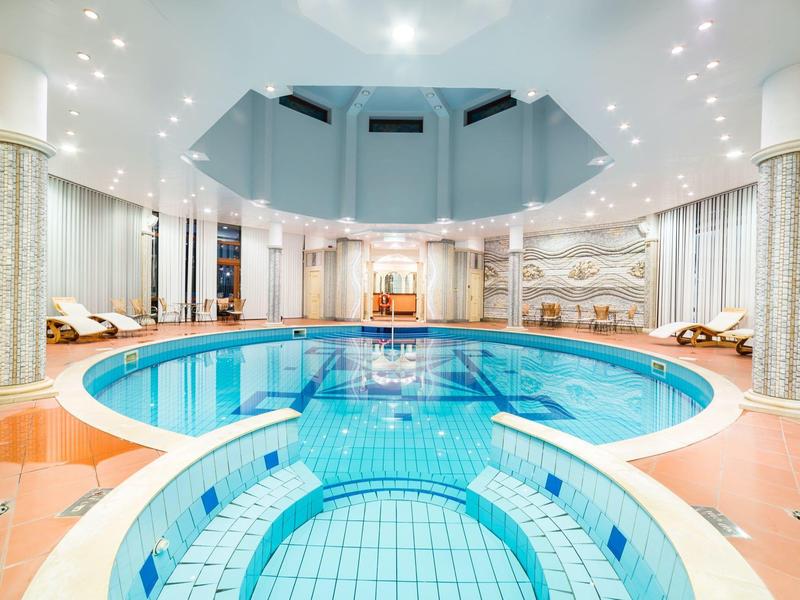 Runder Innenpool mit klarem Wasser, weißen Säulen und hellem Deckendach, umgeben von Liegen.