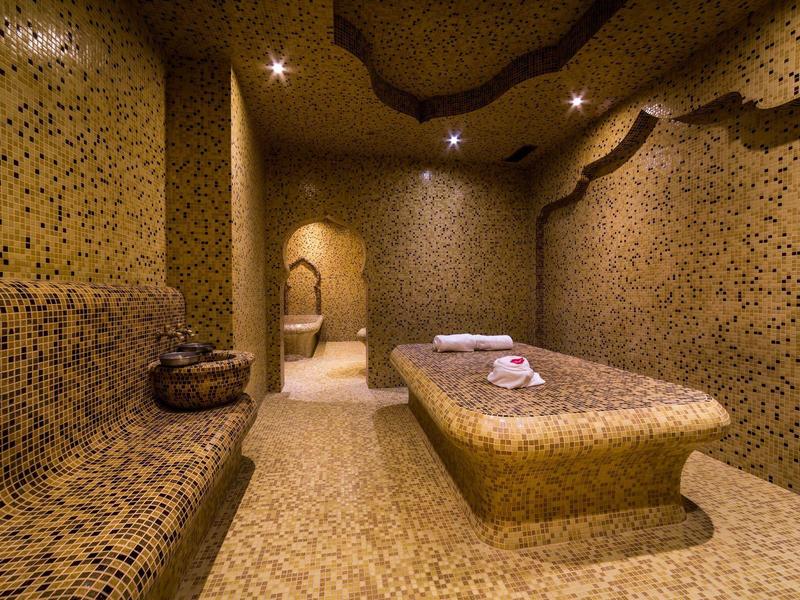 Ein Raum mit Mosaikwänden, einer Liege in der Mitte und gedämpftem, warmem Licht.