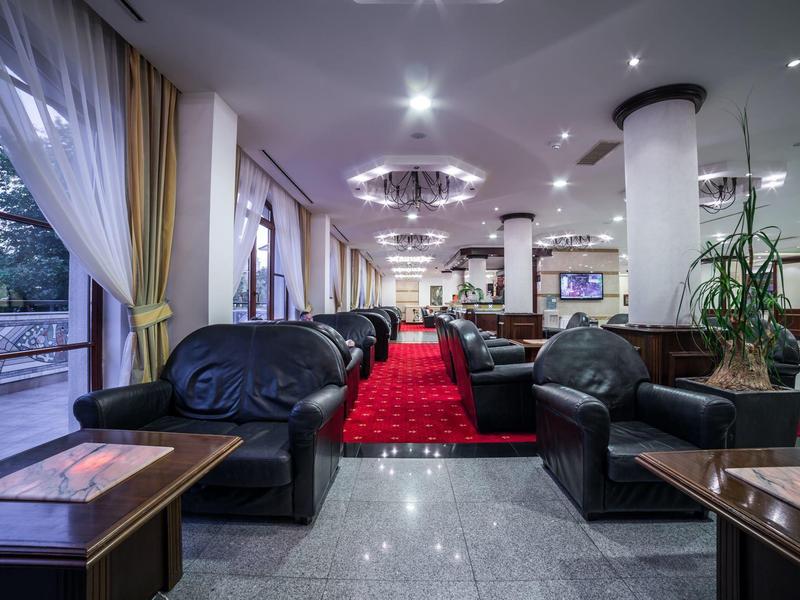 Modernes Hotel-Lobby mit schwarzen Ledersofas, roten Teppichen und großen Fenstern mit weißen Vorhängen.