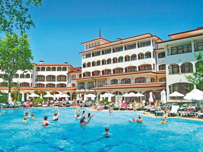 Großer Außenpool vor mehrstöckigem Hotel mit roten Dachziegeln und vielen Gästen im Wasser.