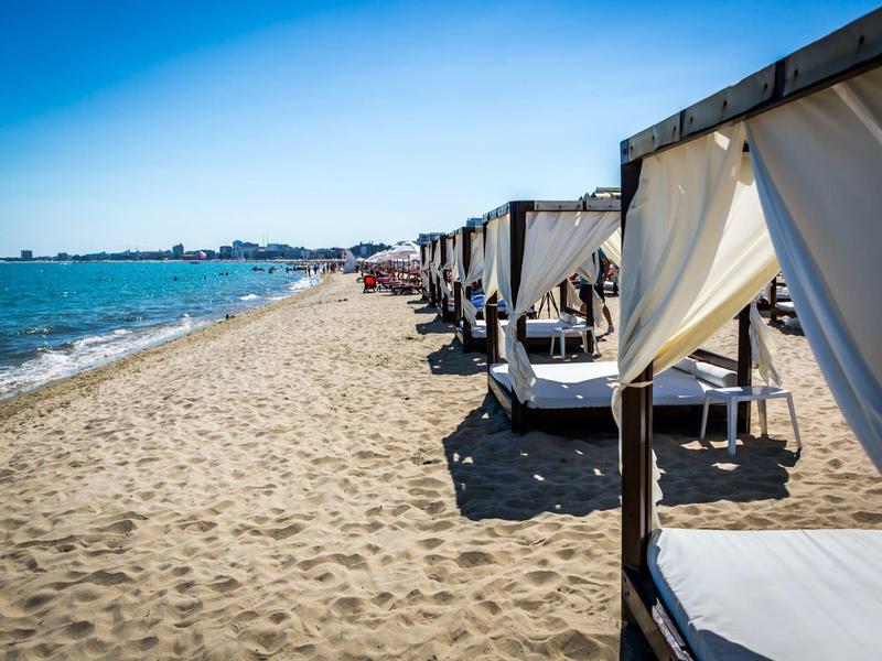 Strand mit Sand, blauer Himmel, Meer und Reihen von weißen Strandbetten mit Vorhängen.