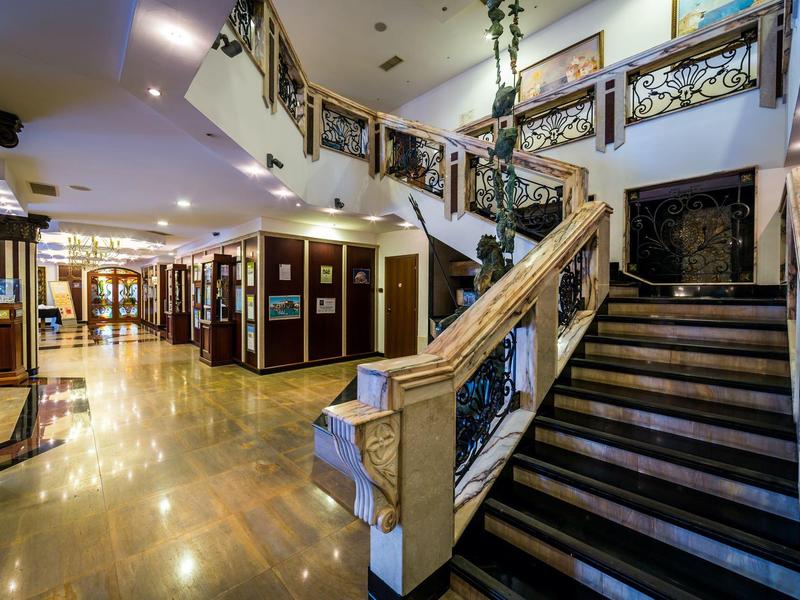 Großer Innenraum mit geschwungener Treppe, goldenen Geländern und glänzendem Marmorboden.