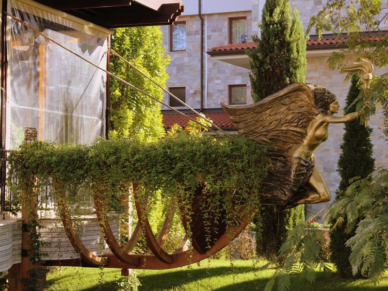 Skulptur eines Bootes mit Vogelkopf und bepflanztem Rumpf aus grünem Efeu vor Hauswand.