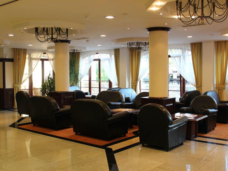 Großer, heller Warteraum mit schwarzen Ledersesseln, großen Fenstern und goldfarbenen Vorhängen.