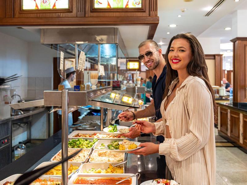 Zwei Personen wählen Essen an einem Buffet mit warmen und frischen Gerichten in heller Kantine.