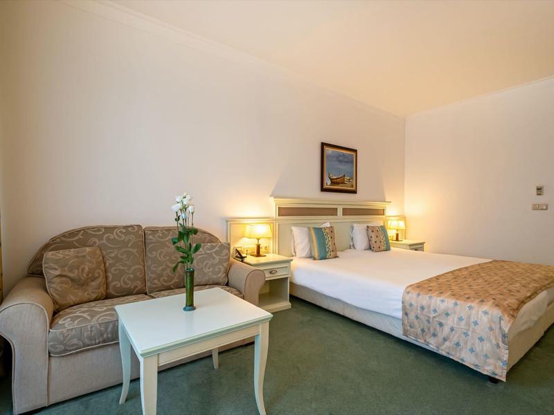 Gemütliches Schlafzimmer mit Doppelbett, Sofa, weißem Tisch und sanfter Beleuchtung.