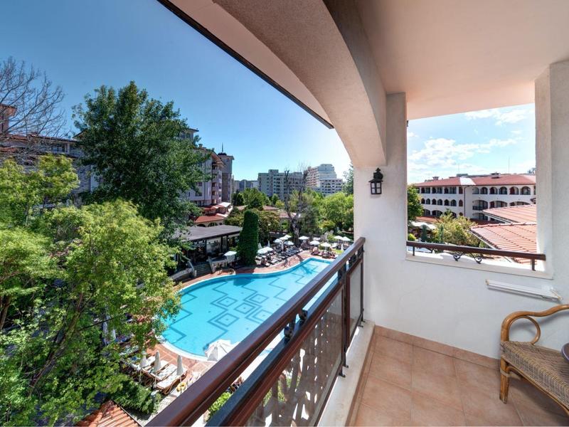 Balkon mit zwei Stühlen, Blick auf Pool, Bäume und umliegende Gebäude bei Sonnenschein.