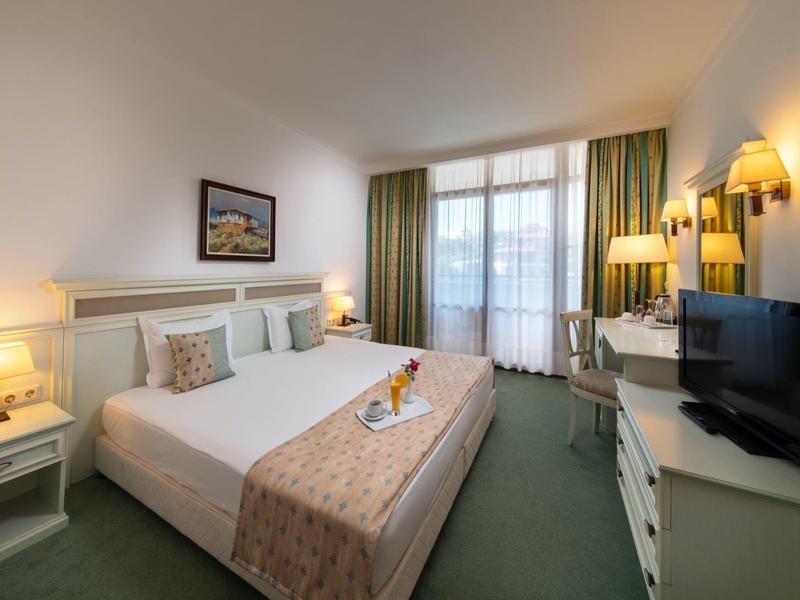 Gemütliches Hotelzimmer mit Doppelbett, Nachttischen, Schreibtisch, Fernseher und Balkonfenster.