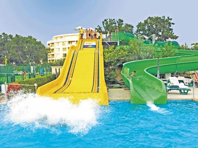 Yellow and green water slides lead into a pool near a hotel and lounge chairs.