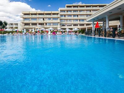Large outdoor pool in front of a multi-story hotel with umbrellas and guests.