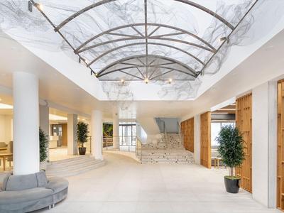 Bright hotel lobby with light stone floor, stone staircase, and glass roof