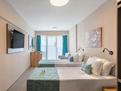 Modern hotel room with two beds, wall-mounted TV, and large window with outside view.