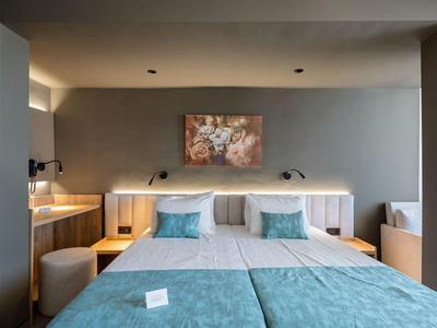 Modern hotel room with two beds, gray walls, and blue pillows and blankets.